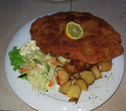Chicken fillet served with potatoes, salad and a lemon on top.