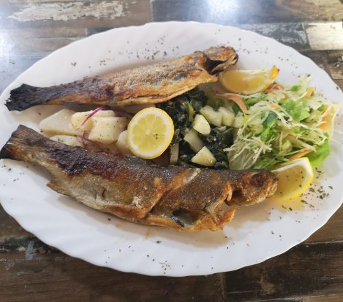 Fried Fish served with lemon on top, lettuce and vegetables on the side.