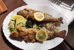 A traditional food. Fried Fish served with lemon on top, lettuce and spinach on the side.