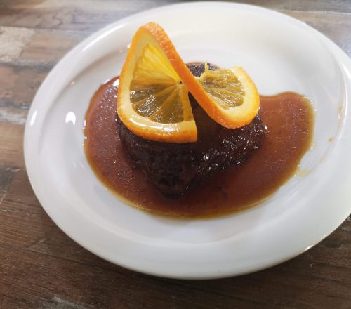 Fig dessert with orange slice on top served in fig jam on white dish.