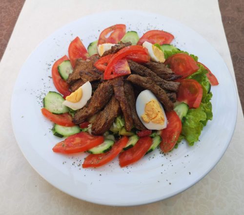 Dish served with meat and boiled eggs carefully placed on top of circular salad made of tomato,cucumber and lettuce.