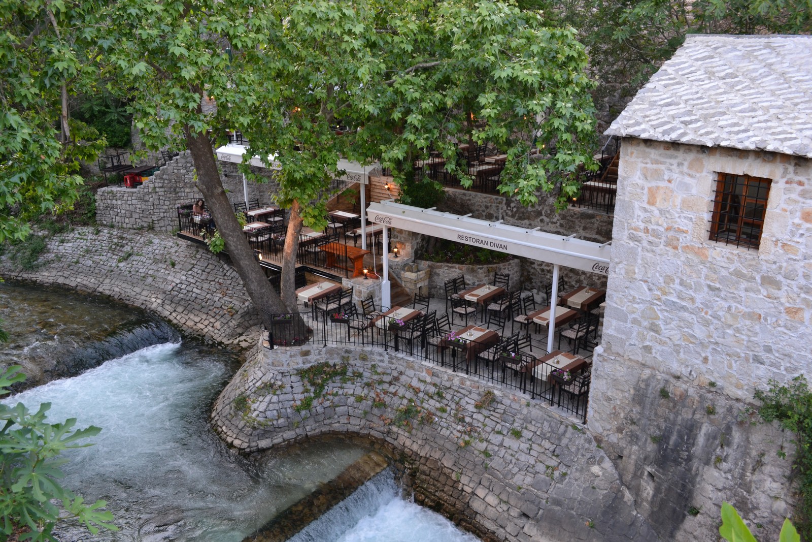 Restaurant terrace with a tree on side and a view on the river. Enclosed by cement walls built in old style.