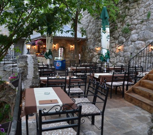 Restaurant terrace and outdoor seating with surrounding trees and old-style walls.