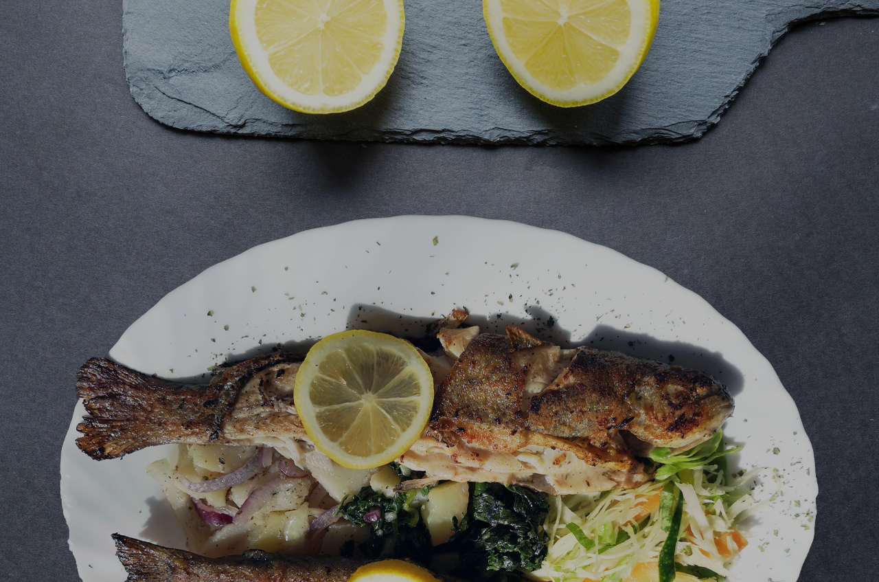 Fish dish served with two fried fishes, salad and lemon slices.